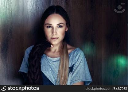 Fashion portrait of a woman with natural makeup strands near wooden background with flare light on it, wearing stylish black knitted gloves, genuine beauty of a woman, femininity and sensuality concept. Genuine beauty of a woman