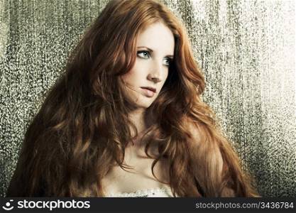 Fashion portrait of a young beautiful redheaded woman on a gold background