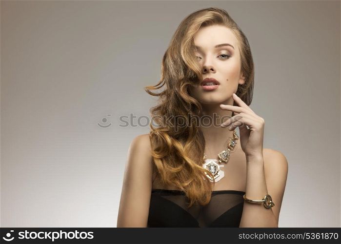 fashion portrait of attractive young girl with elegant wavy hair-style, sexy dress and big golden necklace