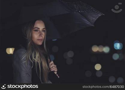 Fashion portrait of beautiful gorgeous woman standing with umbrella under the rain over night city lights background, melancholy concept. Lonely woman at night