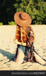 Fashion portrait of beautiful hippie young woman wearing boho chic clothes and summer hat outdoors. Soft warm vintage color tone. Artsy bohemian style.