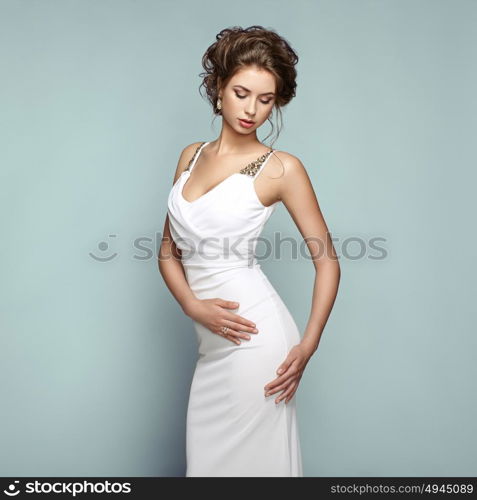 Fashion portrait of beautiful woman in elegant white evening dress. Girl with elegant hairstyle and jewelry