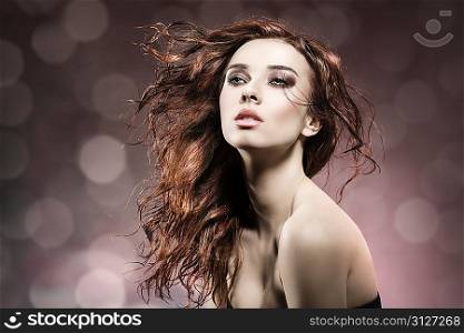 fashion portrait of beuty brunette girl with wavy, flying wet hair. Posing with sensual expression and and cute make-up on flare background