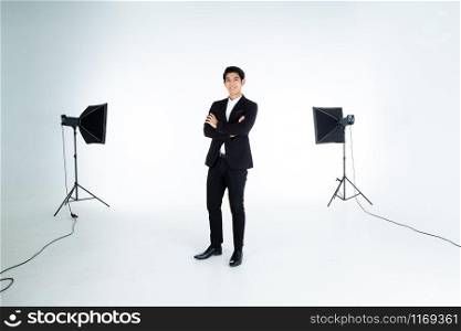 fashion Portrait of handsome young Asian man with arms folded isolated on white grey blank copy space studio showing behind the scenes lights background,indoor studio shoot