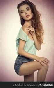 fashion portrait of sensual young woman in sexy pose with her perfect body wearing denim shorts, blue shirt and vintage sunglasses on the head. Stylish make-up, charming expression