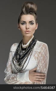 fashion portrait of sexy brunette with elegant hair-style and a lot of necklaces. Wearing white lace shirt and looking in camera