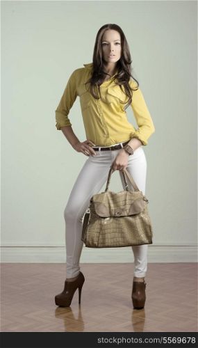 fashion portrait of sexy brunette woman with casual clothes, natural hair style and vogue bag. Wearing yellow shirt, heels and white pants