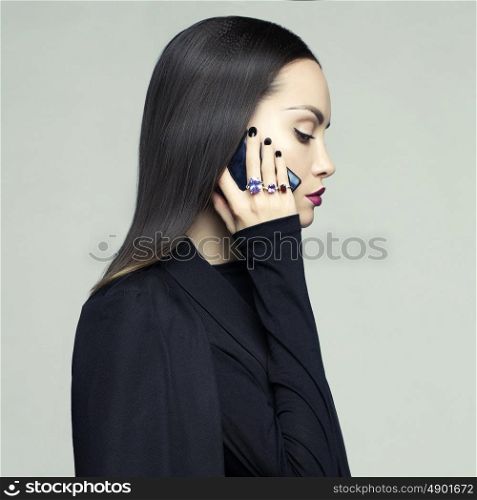 Fashion portrait of stylish woman in black cape talking on her mobile phone. Perfect makeup and manicure. Rings with precious stones