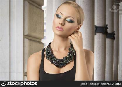 fashion portrait of very pretty woman with elegant style, posing with blonde hair-style, cute blue make-up, dark dress and nice big beads necklace