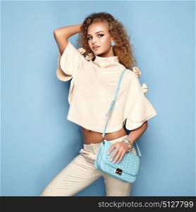 Fashion portrait of woman in summer outfit. Girl posing on blue background. Blue handbag. Stylish curly hairstyle. Glamour lady