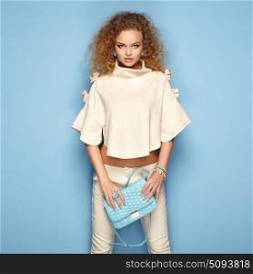 Fashion portrait of woman in summer outfit. Girl posing on pink background. Blue handbag. Stylish curly hairstyle. Glamour lady