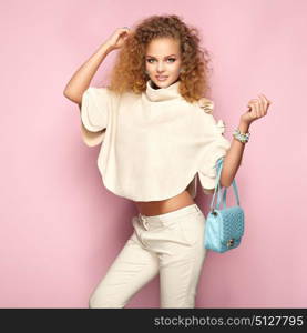Fashion portrait of woman in summer outfit. Girl posing on pink background. Blue handbag. Stylish curly hairstyle. Glamour lady