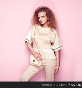 Fashion portrait of woman in summer outfit. Girl posing on pink background. Pink handbag. Stylish curly hairstyle. Glamour lady