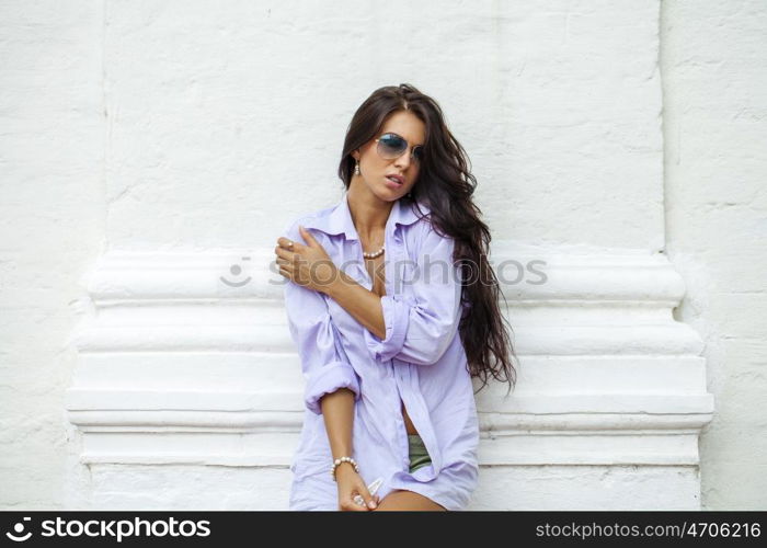 Fashion portrait of young brunette model posing by the brick white wall