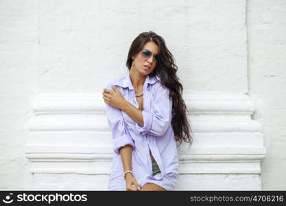 Fashion portrait of young brunette model posing by the brick white wall