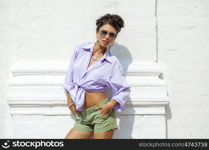 Fashion portrait of young brunette model posing by the brick white wall