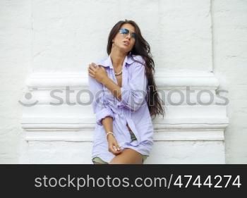 Fashion portrait of young brunette model posing by the brick white wall