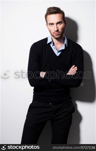 Fashion portrait of young man in black pullover and blue shirt with crossed arms.