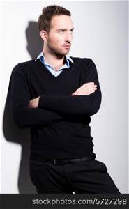 Fashion portrait of young man in black pullover and blue shirt with crossed arms.