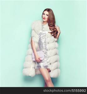 Fashion Portrait Young Woman in white Fur Coat. Girl with Elegant Hairstyle Posing on a Colored Background. Lady Posing in Eco-Fur Coat. Beautiful Luxury Winter Woman. Fashion Model in Silver Dress