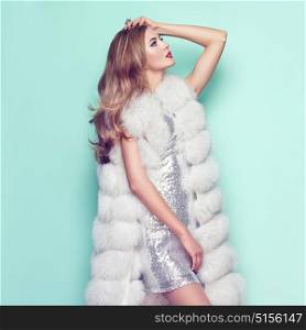 Fashion Portrait Young Woman in white Fur Coat. Girl with Elegant Hairstyle Posing on a Colored Background. Lady Posing in Eco-Fur Coat. Beautiful Luxury Winter Woman. Fashion Model in Silver Dress