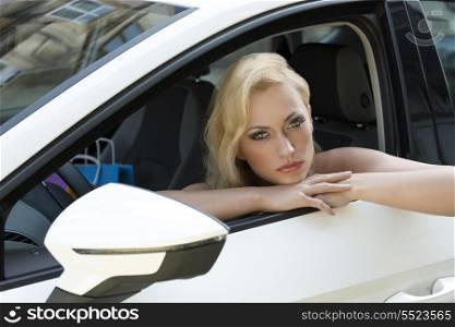 fashion shoot of cute blonde woman sitting in a white car with colorful shopping bag near and sensual eyes
