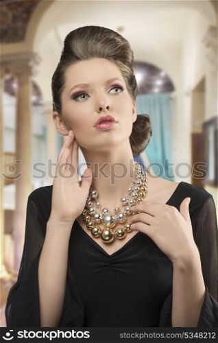 fashion shoot of pretty young brunette girl with elegant style, beautiful hair-style, black dress and big necklace