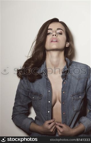 fashion shoot of sensual brunette woman with casual modern style, long natural hair and denim shirt. She is looking in camera