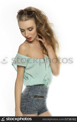 fashion shoot of sensual female with long curly hair, stylish make-up, denim shorts, blue shirt and vintage sunglasses on the head.