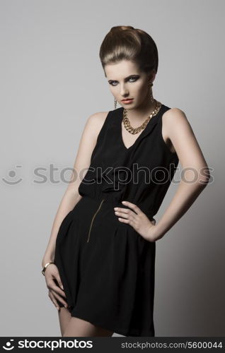 fashion shoot of young elegant girl with cute hair-style and make-up, black dress and golden jewellery