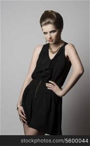 fashion shoot of young elegant girl with cute hair-style and make-up, black dress and golden jewellery