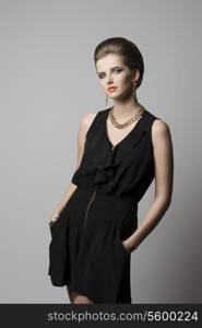 fashion shoot of young elegant girl with cute hair-style and make-up, black dress and golden jewellery