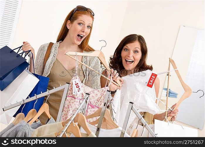 Fashion shopping - Two happy young woman choose clothes in shop holding shopping bag