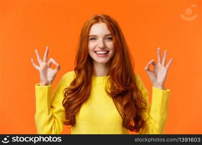 Fashion, shopping, winter holidays concept. Attractive cheerful redhead woman showing okay gestures and smiling, everything alright, approve or like product, recommend online store, orange background.. Fashion, shopping, winter holidays concept. Attractive cheerful redhead woman showing okay gestures and smiling, everything alright, approve or like product, recommend online store, orange background