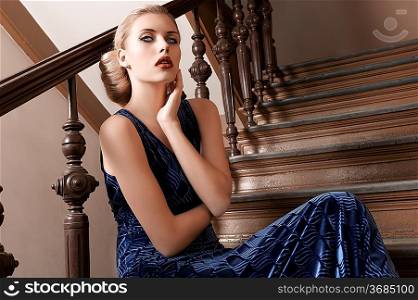 fashion shot of a young and pretty girl in blue long elegant dress sitting on a old fashion stairwell