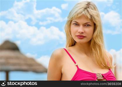 Fashion shot of beautiful blond woman wearing a pink top standing on beach