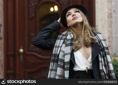 fashion shot of pretty young woman near e old fashion door , she is looking up to the sky , wearing scarf and hat . freckles on face