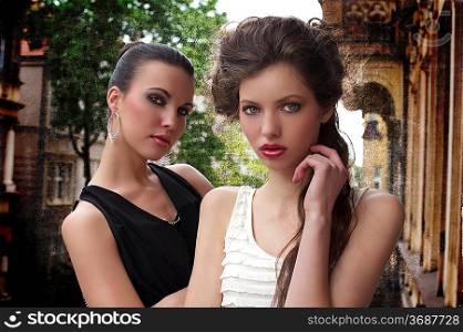 fashion shot of two attractive and elegant girl friend outside in a balcony with old fashion style building in background