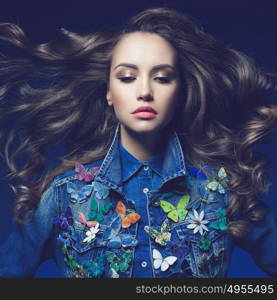 Fashion studio photo of young beauty woman with a lot of brooches on her jeans jacket. Denim clothes. Jeans trend. Magnificent hair