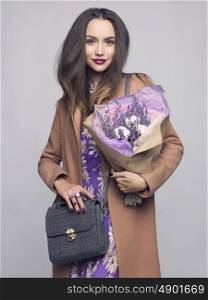 Fashion studio photo of young stylish woman. Beige coat, textile bag, lilac dress, bouquet of lavender. Catalogue clothes and accessories. Lookbook