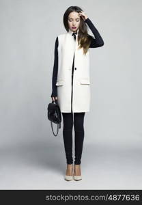 Fashion studio photo of young stylish woman. Elegant beige vest, black jeans and handbag, beige shoes. Catalogue clothes. Lookbook