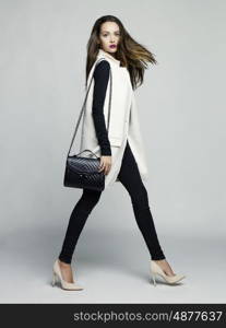 Fashion studio photo of young stylish woman. Elegant beige vest, black jeans and handbag, beige shoes. Catalogue clothes. Lookbook
