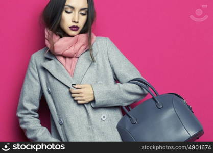 Fashion studio photo of young stylish woman on fuchsia background. Gray coat, pink scarf, purple lipstick, leather bag, . Catalogue clothes and accessories. Lookbook