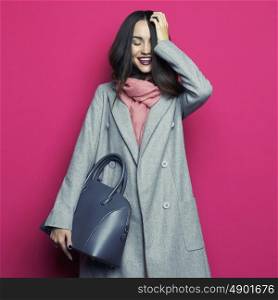 Fashion studio photo of young stylish woman on fuchsia background. Gray coat, pink scarf, purple lipstick, leather bag, . Catalogue clothes and accessories. Lookbook