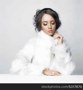 Fashion studio portrait of beautiful lady with elegant hairstyle in white fur coat. Winter beauty in luxury. Fashion fur. Beautiful woman in luxury fur coat. Fashion model posing in eco-fur coat