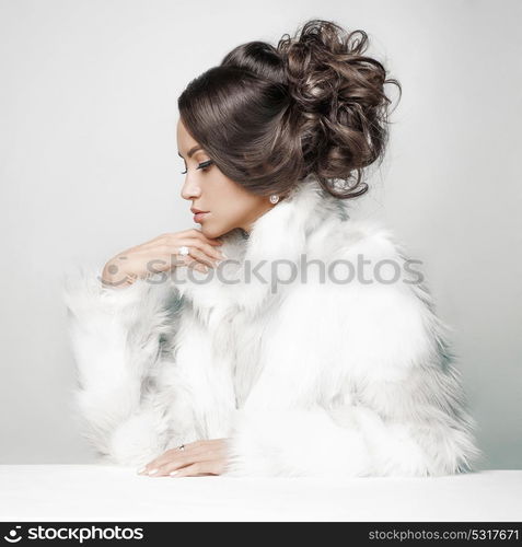 Fashion studio portrait of beautiful lady with elegant hairstyle in white fur coat. Winter beauty in luxury. Fashion fur. Beautiful woman in luxury fur coat. Fashion model posing in eco-fur coat