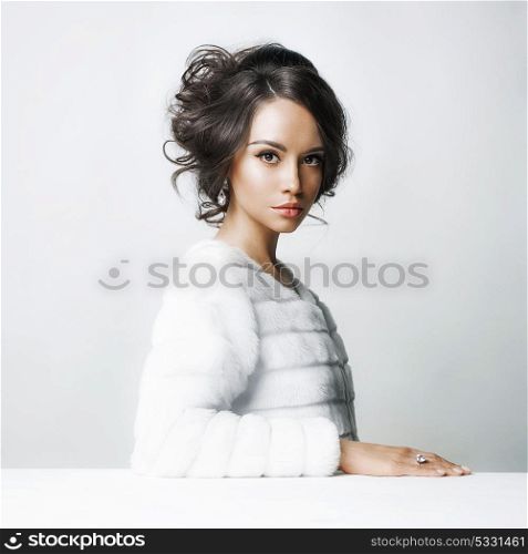 Fashion studio portrait of beautiful lady with elegant hairstyle in white fur coat. Winter beauty in luxury. Fashion fur. Beautiful woman in luxury fur coat. Fashion model posing in eco-fur coat