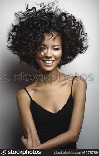 Fashion studio portrait of beautiful smiling woman in black dress with afro curls hairstyle. Fashion and beauty