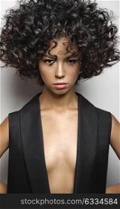 Fashion studio portrait of beautiful woman in black vest with afro curls hairstyle. Fashion and beauty