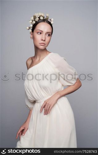 Fashion studio portrait of young beautiful woman in white greek dress with flowers on her head. Fashion and style